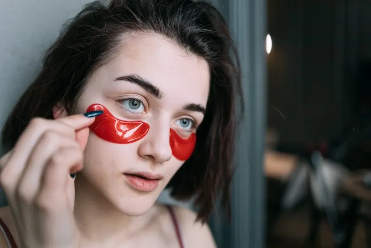 A woman applying a hydrogel patch under her eye.