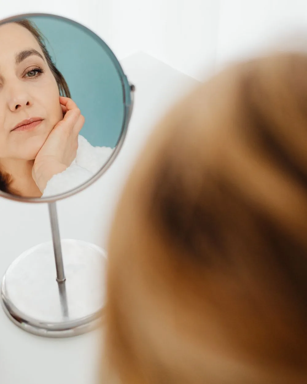 A woman studying her reflection in a hand mirror.