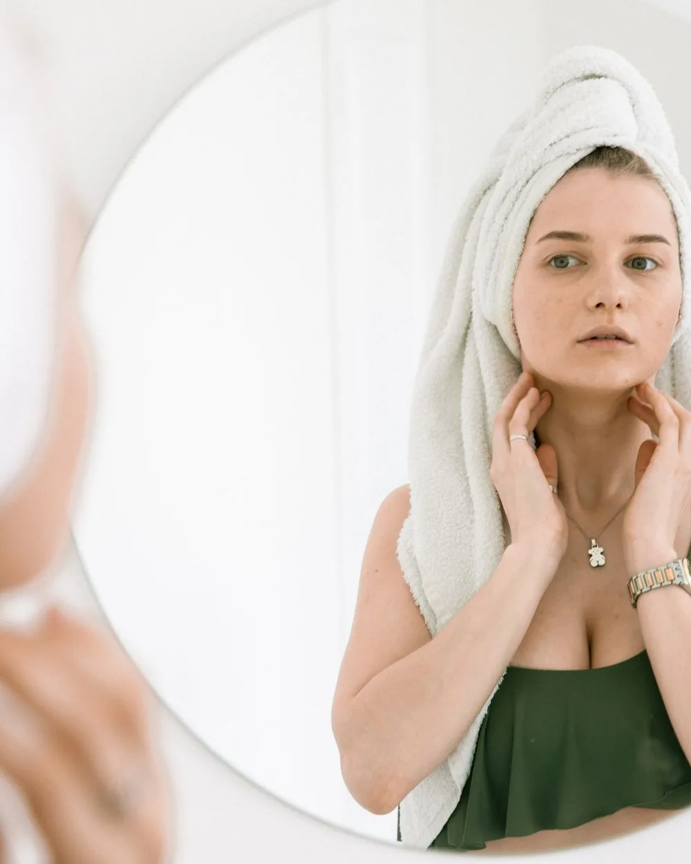 A woman looking at her reflection, hands at her jaw and neck.