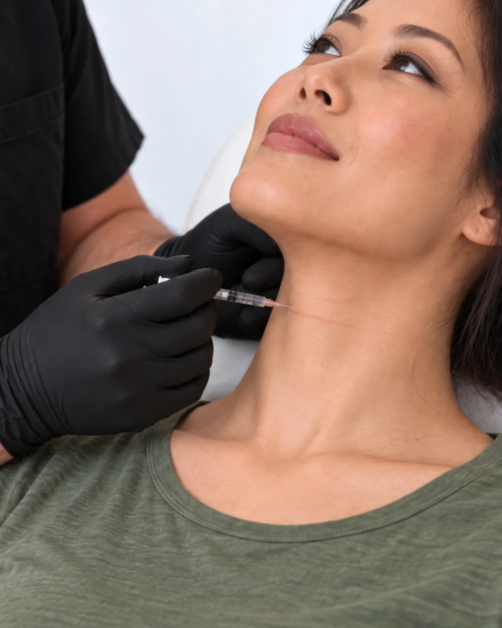 A gloved clinician performing a fine-needle injection to the side of a patient’s neck.
